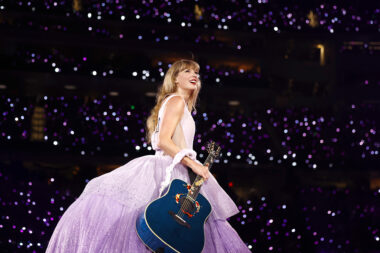 Photo of Taylor Swift in pink and purple dress with blue guitar performing onstage at concert in Inglewood California
